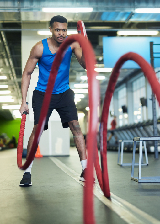 Un joven atleta realizando un entrenamiento intenso con cuerdas de batalla en un gimnasio, representando la importancia de la psicología deportiva para mejorar el rendimiento y la resiliencia en Tres Cantos.