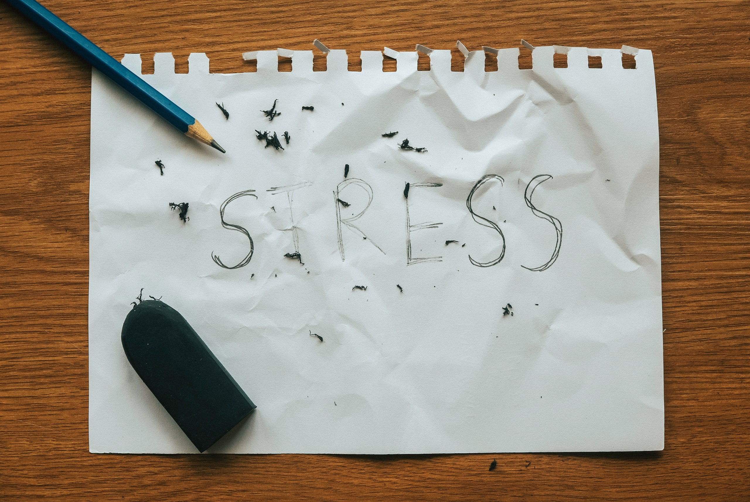 Hoja de papel arrugada con la palabra "stress" escrita, rodeada de restos de goma de borrar y un lápiz roto, representando el manejo del estrés laboral.