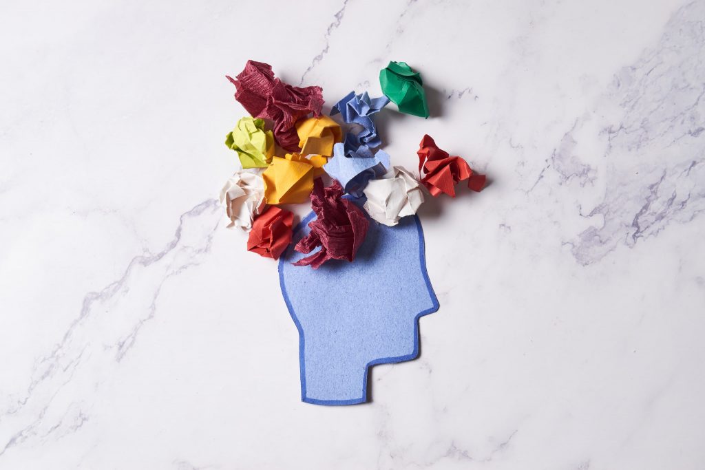 Figura de cabeza hecha de papel azul con papeles arrugados de colores, simbolizando el diagnóstico de los trastornos de ansiedad y los pensamientos desordenados.
