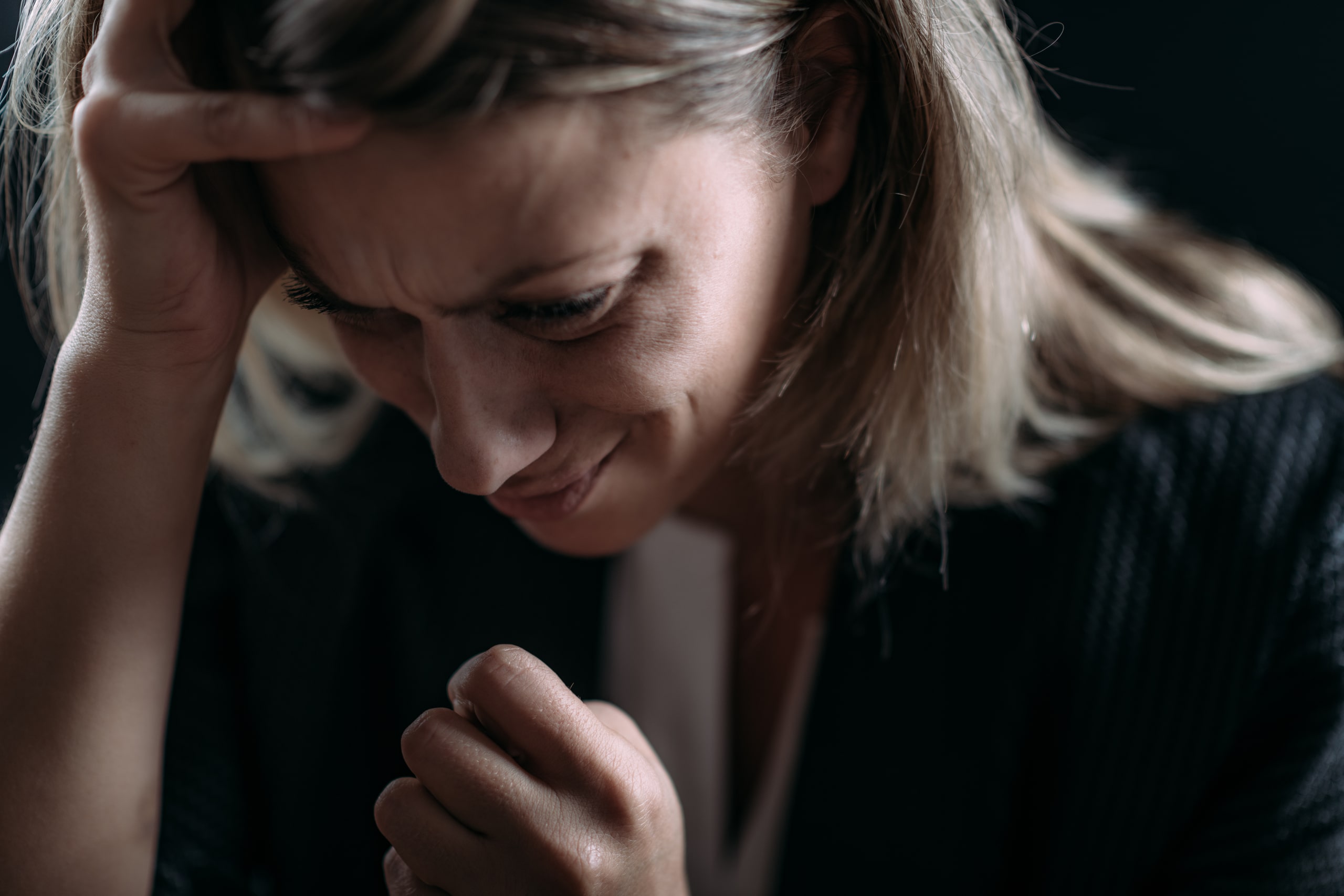 Mujer con gesto de angustia y mano apoyada en la cabeza, representando síntomas comunes del trastorno por estrés postraumático como el miedo, la ansiedad y el estrés emocional.