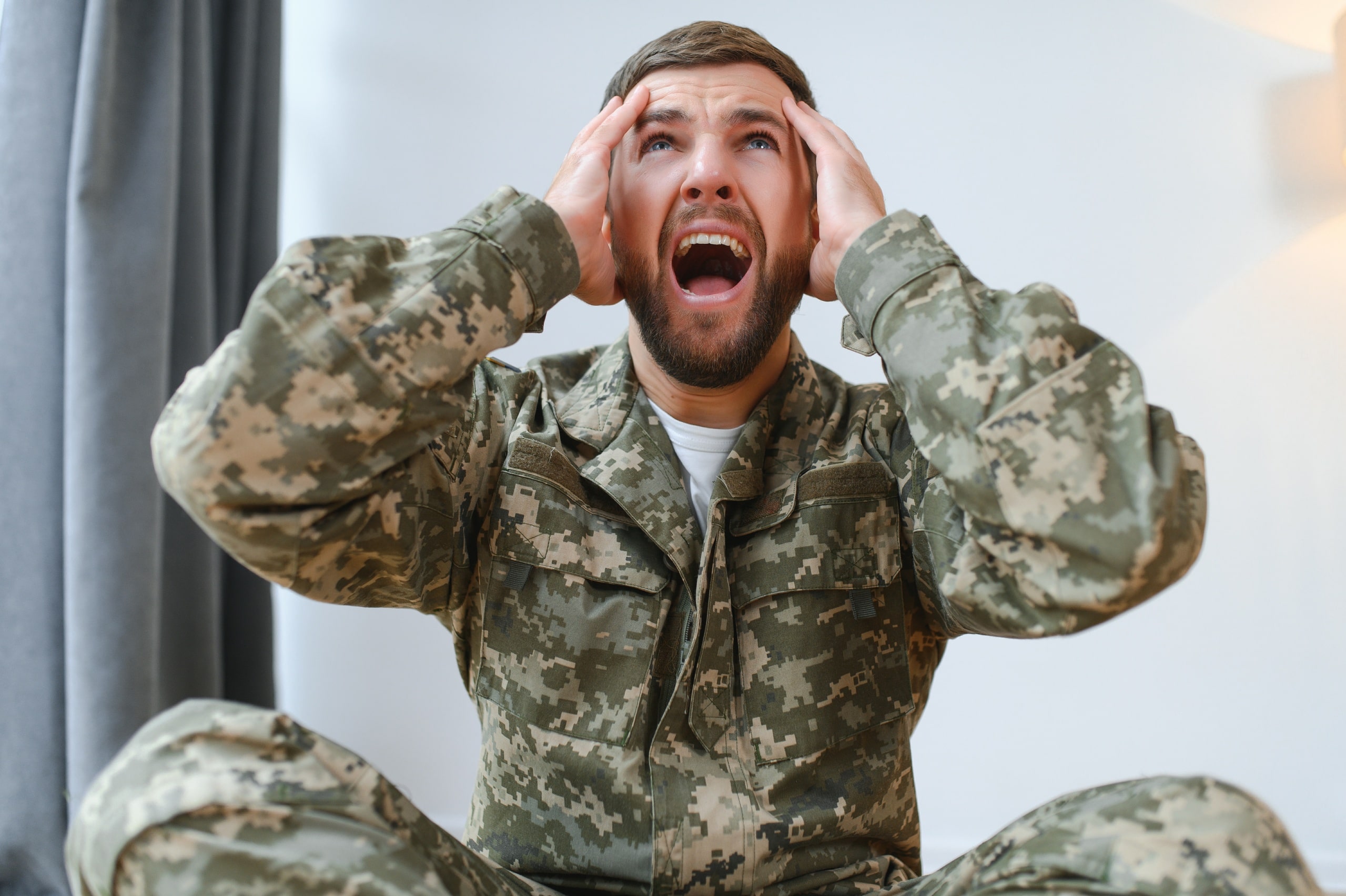 Militar sentado en el suelo con expresión de estrés y las manos sobre la cabeza, representando el proceso de diagnóstico del trastorno por estrés postraumático (TEPT) en personas expuestas a experiencias traumáticas.