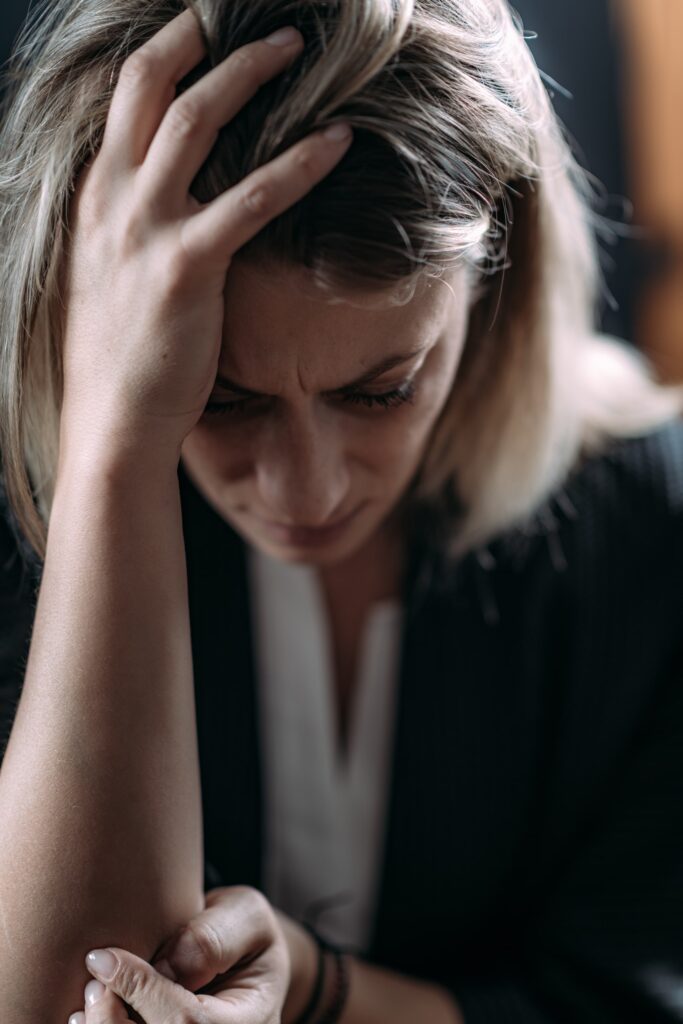 Primer plano de una mujer con gesto de preocupación, sosteniéndose la cabeza y el brazo, representando los síntomas físicos del trastorno de ansiedad generalizada, como tensión y estrés.