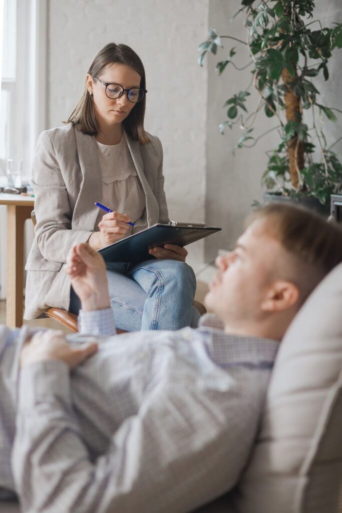 Psicoterapeuta tomando notas mientras escucha a un paciente recostado en un sofá, representando un tratamiento efectivo para la ansiedad generalizada mediante terapia profesional.