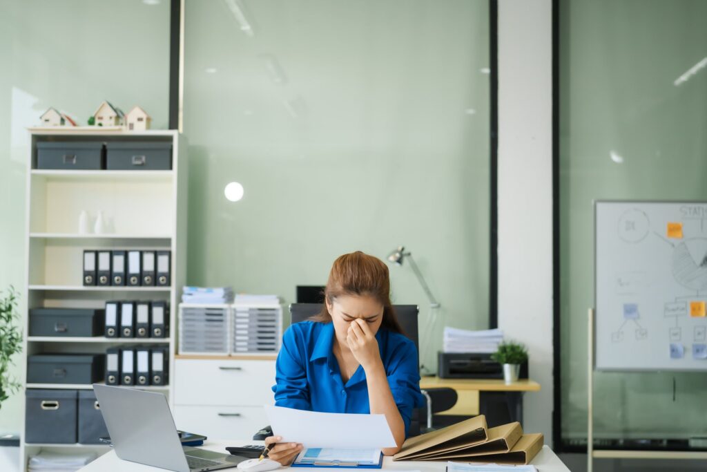 Mujer trabajando en un escritorio de oficina rodeada de documentos y una computadora, representando las posibles causas del estrés laboral como la sobrecarga de trabajo y la presión profesional.